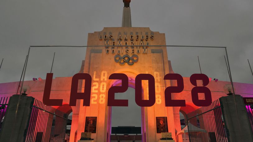 FILE - An LA 2028 sign is seen in front of the Olympic cauldron at the Los Angeles Memorial Coliseum, Wednesday, Sept. 13, 2017. The 2028 Los Angeles Olympics have announced more venue assignments, with the cities of Carson and Long Beach reprising their roles from previous games held in the region. (AP Photo/Richard Vogel, File)