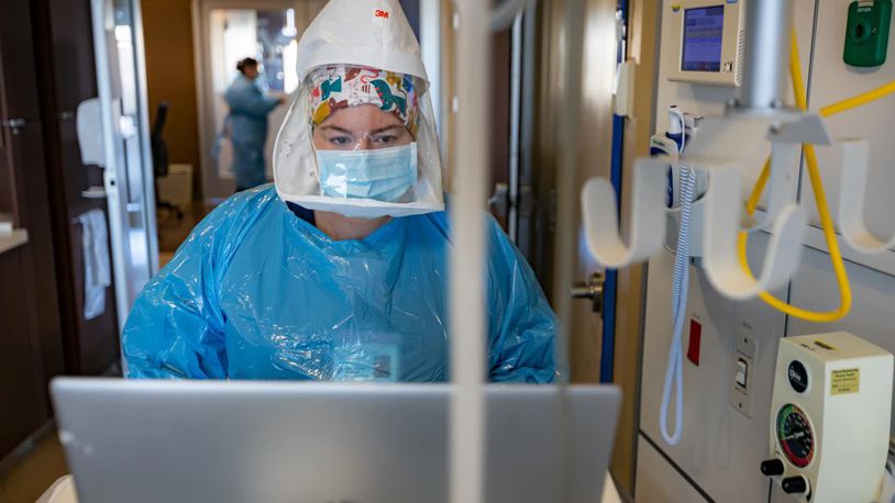 In this file photo, Taylor Spicer, a nurse at Miami Valley Hospital, is wearing full personal protective equipment, including an oxygen tank on her back, as she enters data for a COVID-19 patient in the hospital's COVID-19 unit.