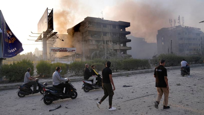 People pass in front of destroyed buildings that were hit by Israeli airstrikes in Dahiyeh, Beirut, Lebanon, Sunday, Oct. 6, 2024. (AP Photo/Hussein Malla)