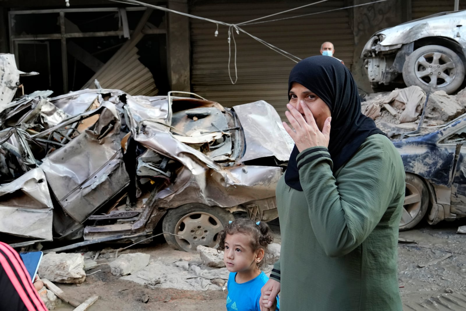 A woman passes in front of destroyed cars at the site of Thursday's Israeli airstrike, in Beirut, Lebanon, Friday, Oct. 11, 2024. (AP Photo/Hussein Malla)