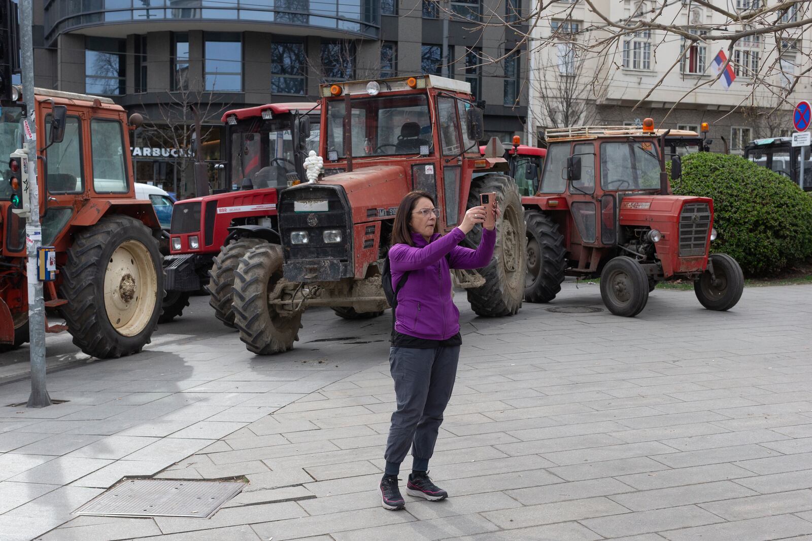 A person takes photos of tractors brought in and parked by supporters of the Serbian president Aleksandar Vucic in Belgrade, Serbia, Friday, March 14, 2025, as the country prepares for a major anti-corruption rally this weekend. (AP Photo/Marko Drobnjakovic)