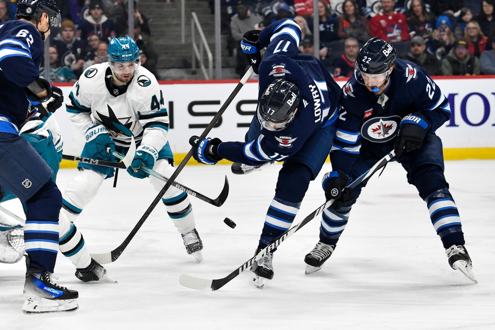 Winnipeg Jets' Adam Lowry (17) and Mason Appleton (22) try to control a bouncing puck as San Jose Sharks' Marc-Edouard Vlasic (44) defends during the second period of an NHL hockey game in Winnipeg, Manitoba, Monday, Feb. 24, 2025. (Fred Greenslade/The Canadian Press via AP)