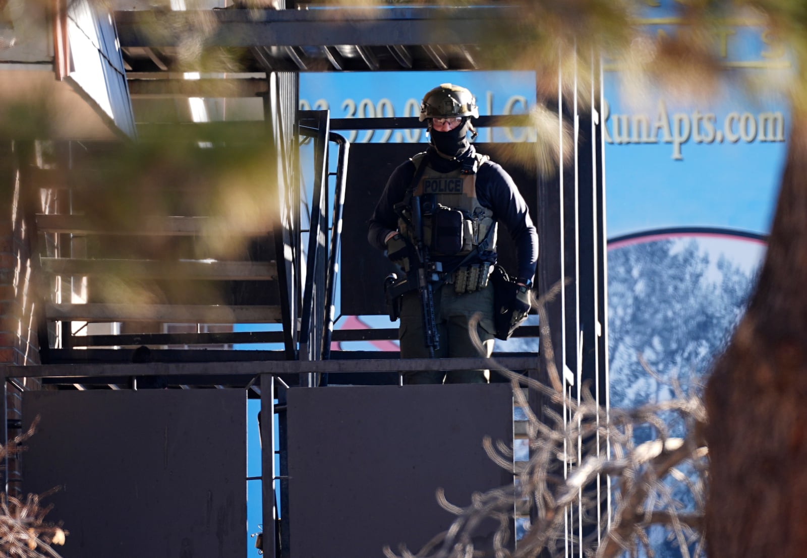 A law enforcement officer stands on a set of stairs outside an apartment complex during a raid Wednesday, Feb. 5, 2025, in east Denver. (AP Photo/David Zalubowski)