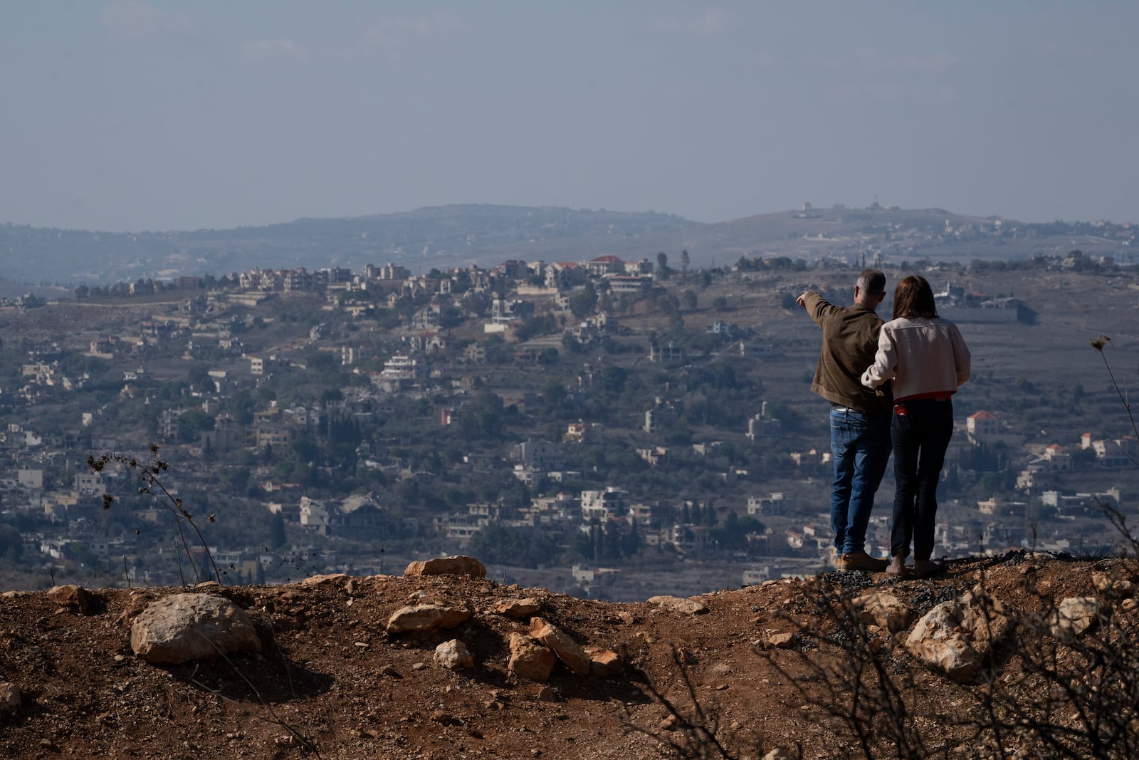 An Israeli couple observe the damaged buildings on a village in southern Lebanon as they stand near the Israeli-Lebanese border, during the ceasefire between Israel and Hezbollah, in the northern Israel, Saturday, Nov. 30, 2024. (AP Photo/Leo Correa)