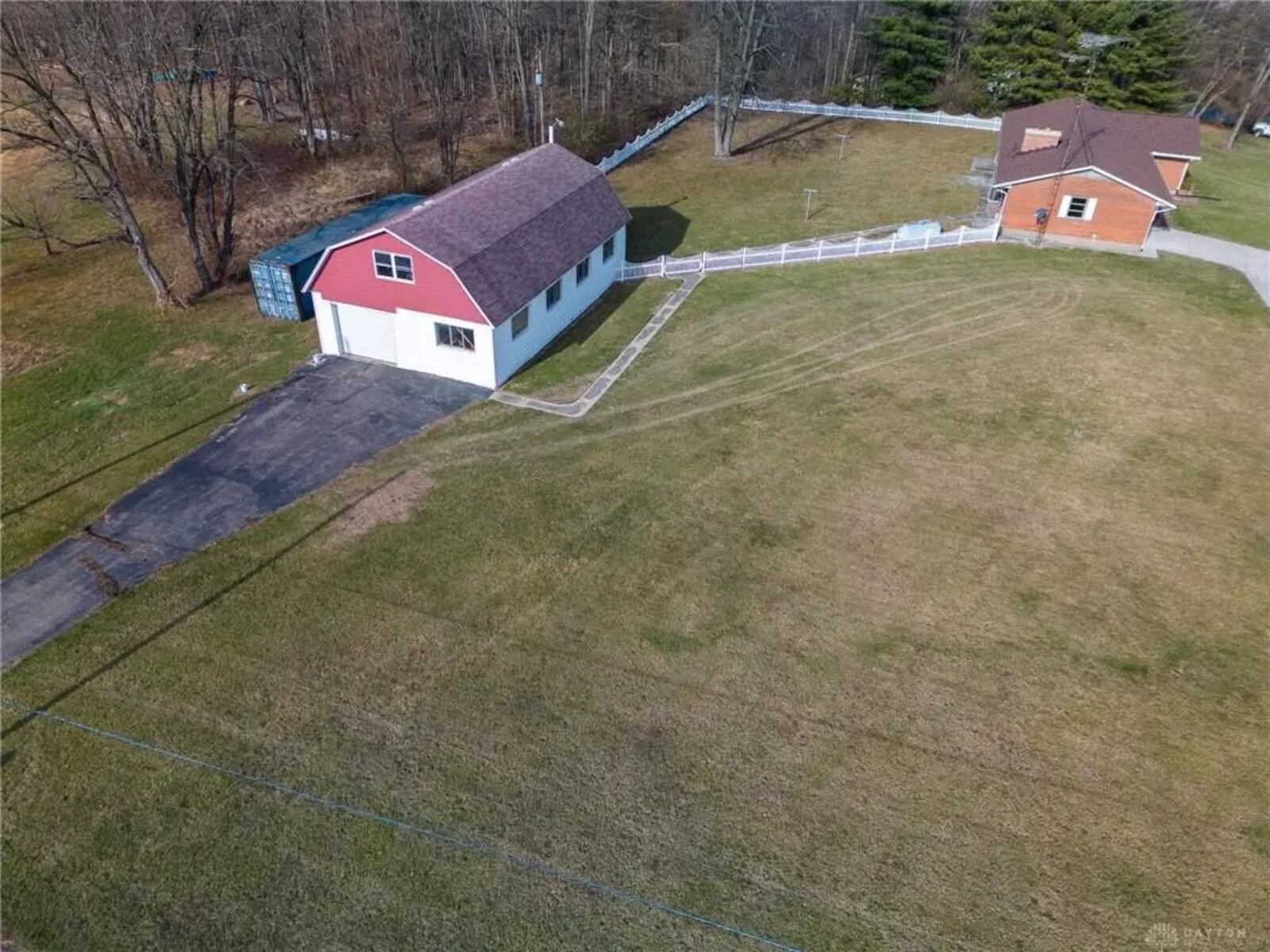 The backyard is partially fenced with wood pickets, and the barn has a separate asphalt driveway. Contributed