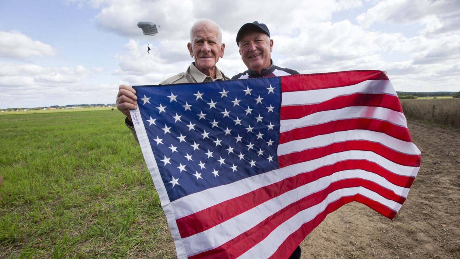 A  98-year-old American WWII veteran, Tom Rice, and U.S. Ambassador Pete Hoekstra, right, pose with the U.S. flag after Rice landed in a tandem parachute jump near Groesbeek, Netherlands, Thursday, Sept. 19, 2019, with the 101st Airborne Division.