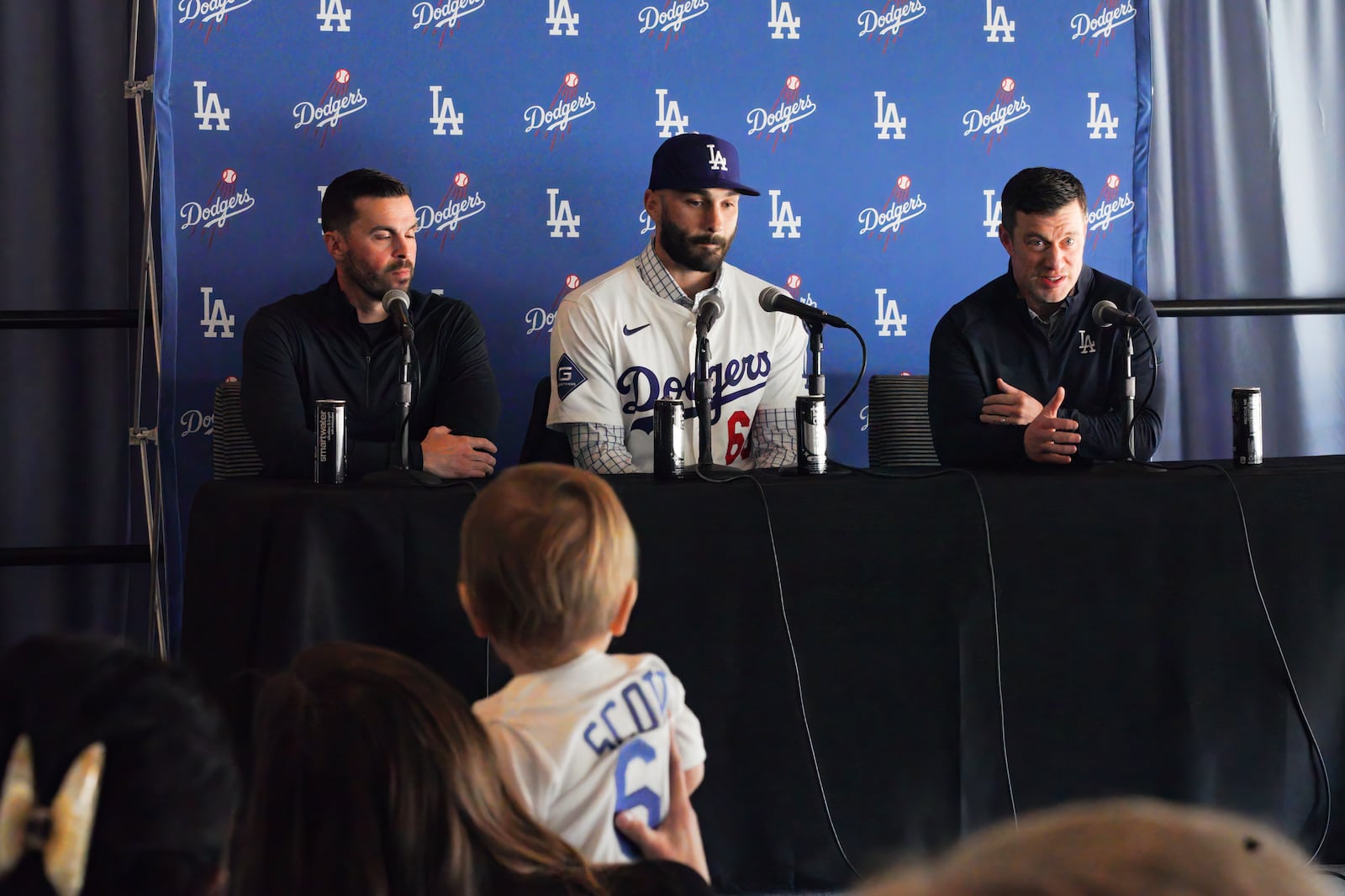 Bo Scott watches as his father Left-handed reliever Tanner Scott, center, is introduced by Andrew Friedman president of baseball operations for the Los Angeles Dodgers, right, and Executive Vice President and General Manager Brandan Gomes, during a news conference at Dodger Stadium in Los Angeles on Thursday, Jan. 23, 2025. (AP Photo/Richard Vogel)