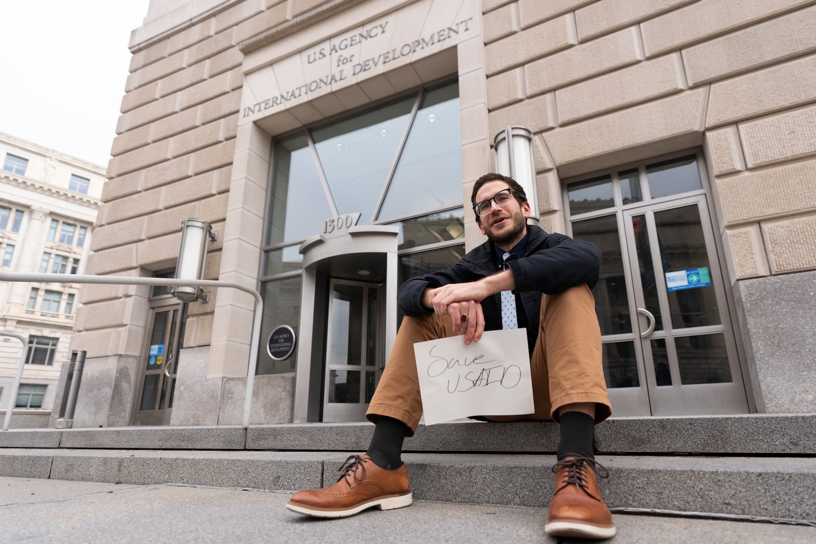 A United States Agency for International Development, or USAID, contract worker sits in front of the USAID office with a message written on a piece of paper, Monday, Feb. 3, 2025, in Washington (AP Photo/Manuel Balce Ceneta)