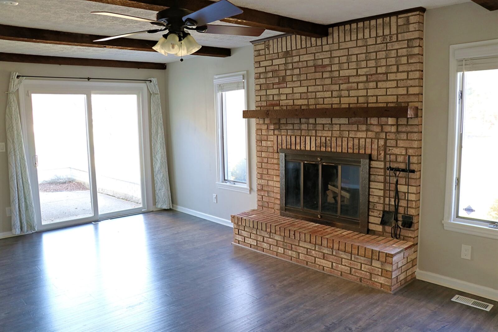 The fireplace, which has a raised brick hearth, is flanked by two windows and large sliding patio doors provide additional natural lighting.