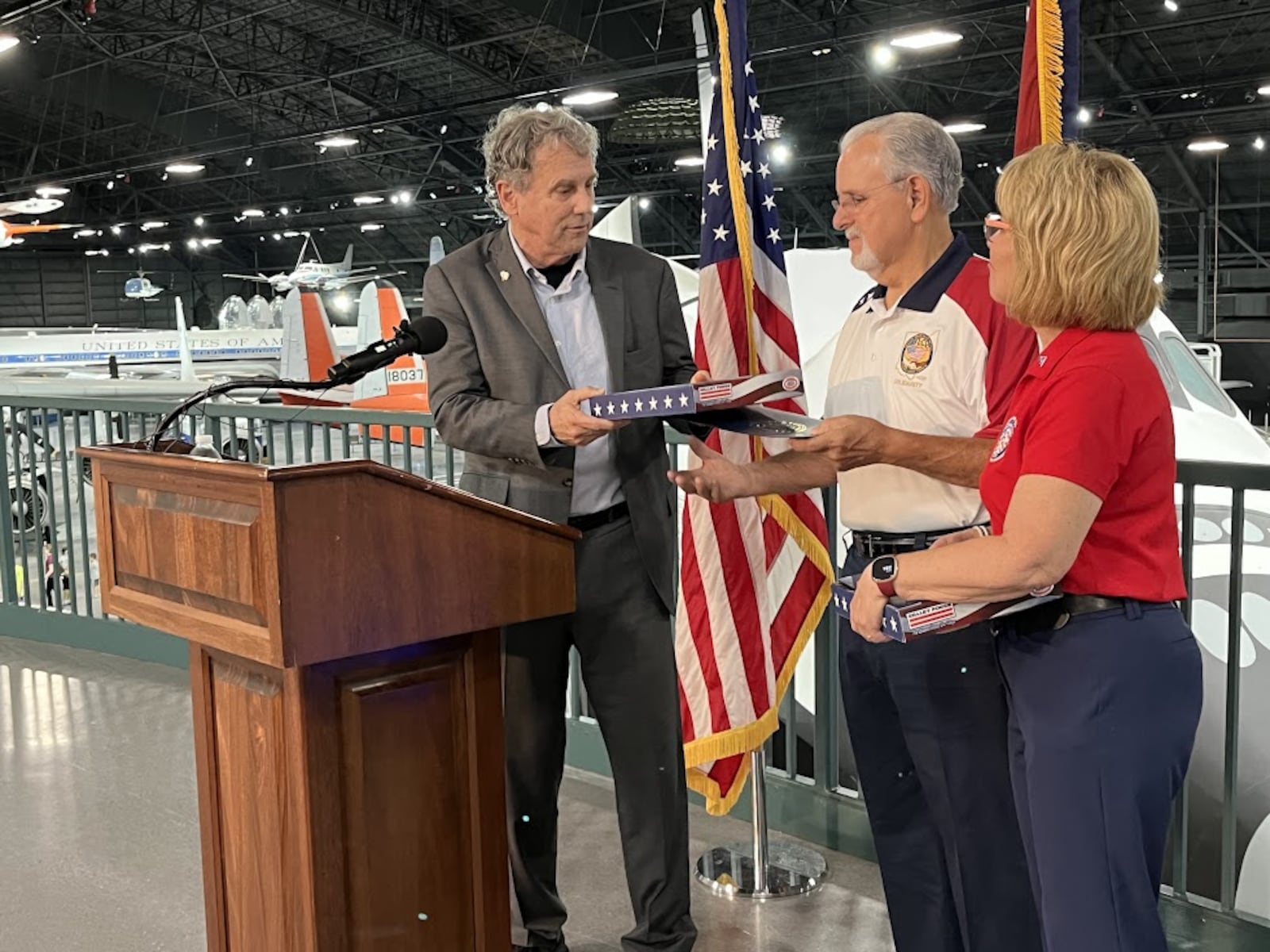 U.S. Sen. Sherrod Brown, D-Ohio, hands Tom Ritchie, president of the Dayton-Miami Valley Regional Labor Council, a flag that has flown over the U.S. Capitol on Wednesday, Aug. 7, 2024, at the National Museum of the U.S. Air Force. Next to Ritchie is Kim Frisco, executive director of the Montgomery County Veterans Services Commission. THOMAS GNAU/STAFF