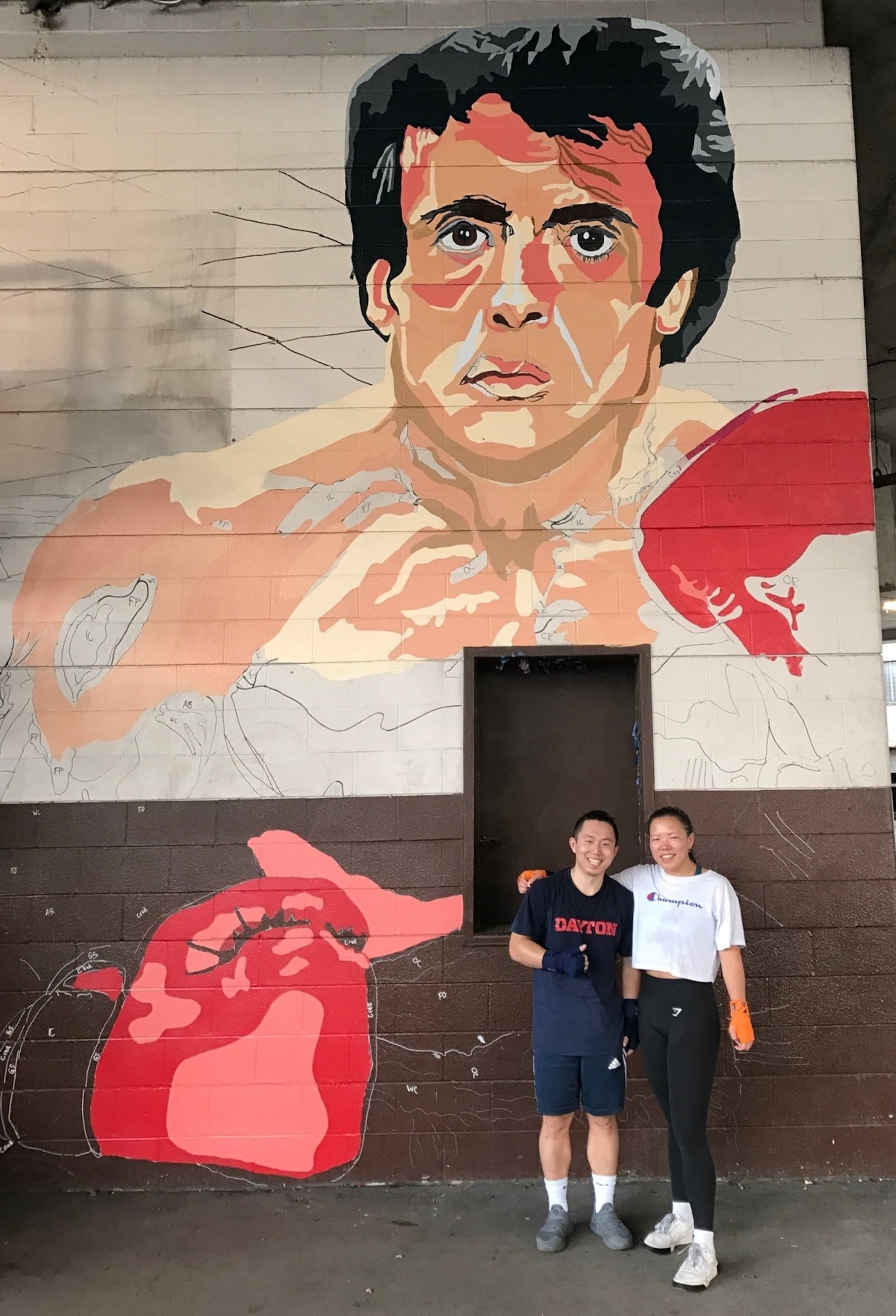 Hyde Li and Grace Ashworth in front of the large Rocky Balboa and Apollo Creed mural being painted on the side of Drake’s Downtown Gym by artists from the nearby K12 Gallery & TEJAS on Jefferson Street. Tom Archdeacon/STAFF