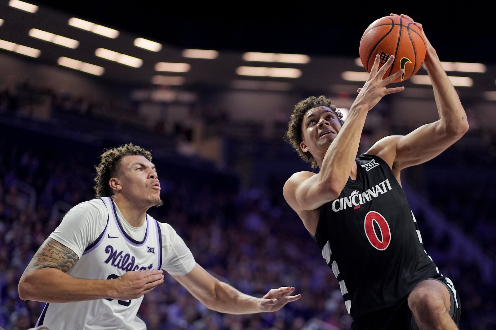 Cincinnati guard Dan Skillings Jr. (0) gets past Kansas State guard Coleman Hawkins to put up a shot during the first half of an NCAA college basketball game, Monday, Dec. 30, 2024, in Manhattan, Kan. (AP Photo/Charlie Riedel)