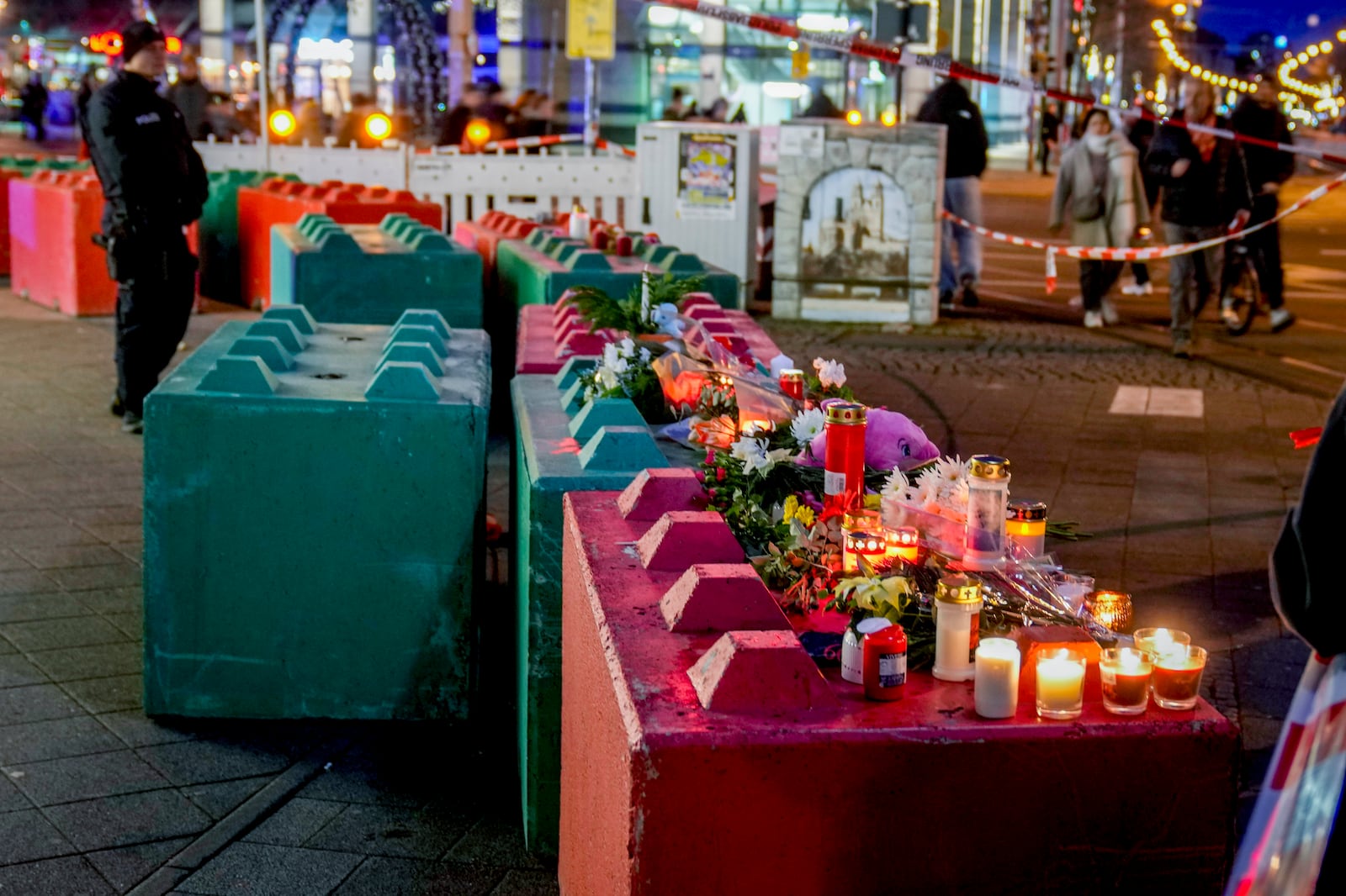 People lay flowers and light candles on concrete blocks that protect the Christmas market, where a car drove into a crowd on Friday evening, in Magdeburg, Germany, Saturday, Dec. 21, 2024. (AP Photo/Michael Probst)