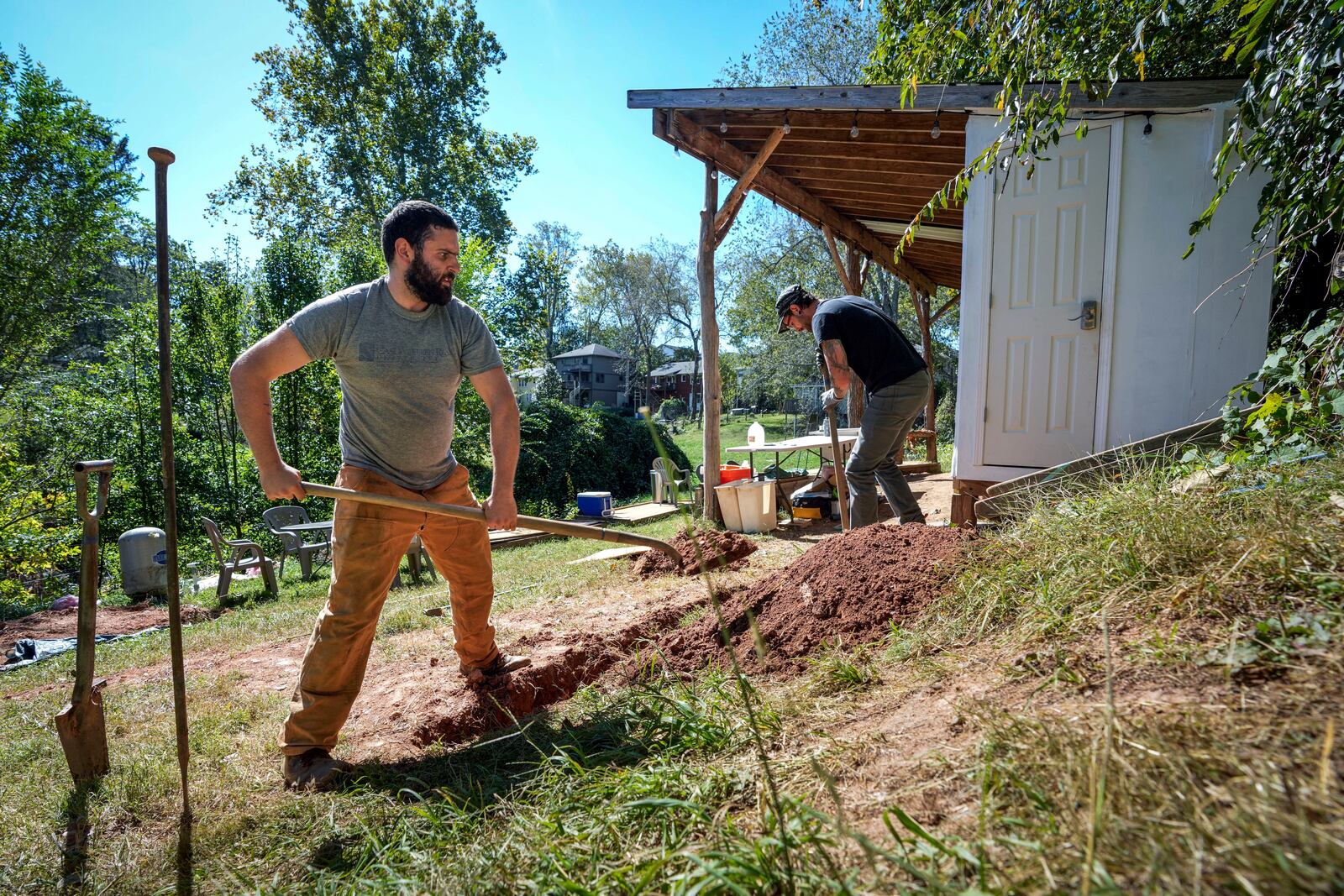 Volunteers, Ben Gordon, left, and Anthony Rubino work on digging a ditch for pipes to offer both nonpotable and potable water for the community, Monday, Oct. 14, 2024, in Asheville, N.C. (AP Photo/Kathy Kmonicek)