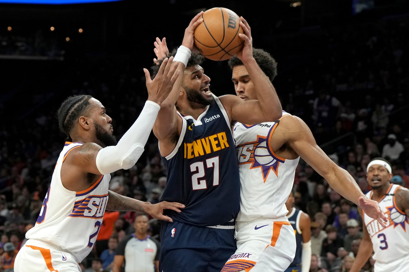 Denver Nuggets guard Jamal Murray drives between Phoenix Suns guard Monte Morris and center Oso Ighodaro during the first half of an NBA basketball game, Wednesday, Dec. 25, 2024, in Phoenix. (AP Photo/Rick Scuteri)