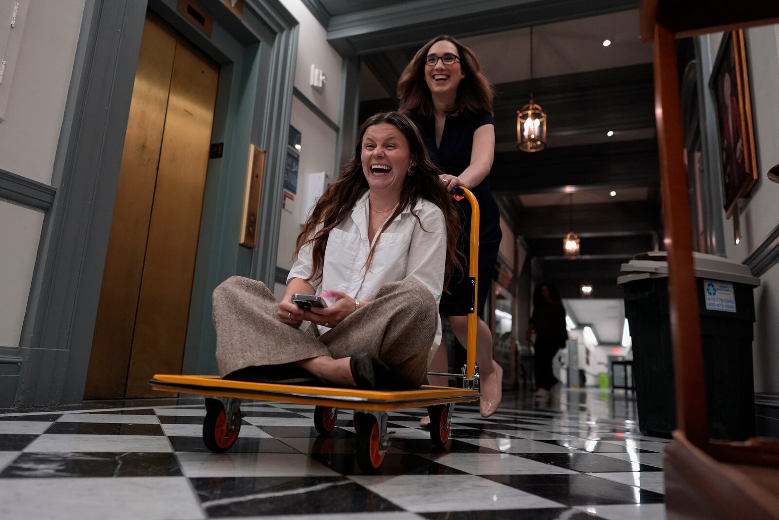 U.S.-Rep.-elect Sarah McBride, D-Del., speeds her incoming Deputy Chief of Staff and Communications Director, Michaela Kurinsky-Malos, through the halls of Delaware Legislative Hall on a moving cart as they move out of McBride's Delaware state senate office in Dover, Del., Tuesday, Dec. 17, 2024. (AP Photo/Carolyn Kaster)