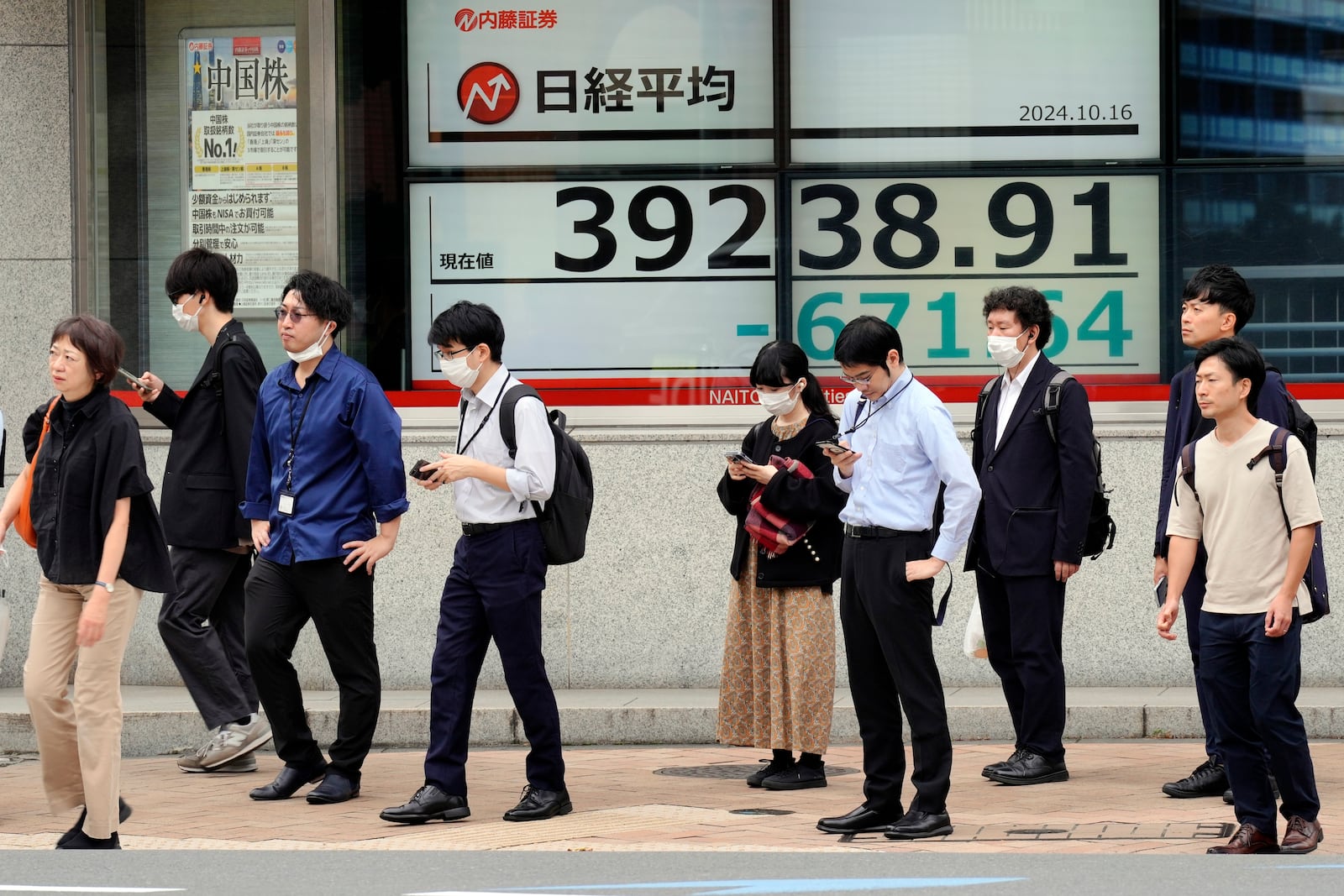 People stand in front of an electronic stock board showing Japan's Nikkei index at a securities firm Wednesday, Oct. 16, 2024, in Tokyo. (AP Photo/Eugene Hoshiko)