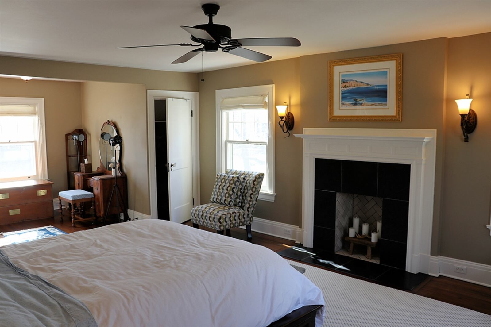 The main bedroom mirrors the size of the living room below and has a decorative fireplace with marble surround and a dentil wood mantel. Large windows fill the room with natural light and the bold molding complements the wood floor. 