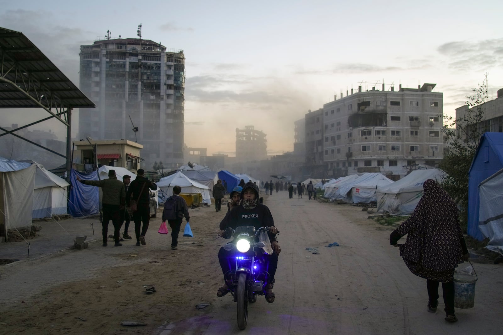 Palestinians walk and drive past tents shortly after an Israeli army airstrike nearby, in central Gaza City, Saturday, March 22, 2025. (AP Photo/Jehad Alshrafi)