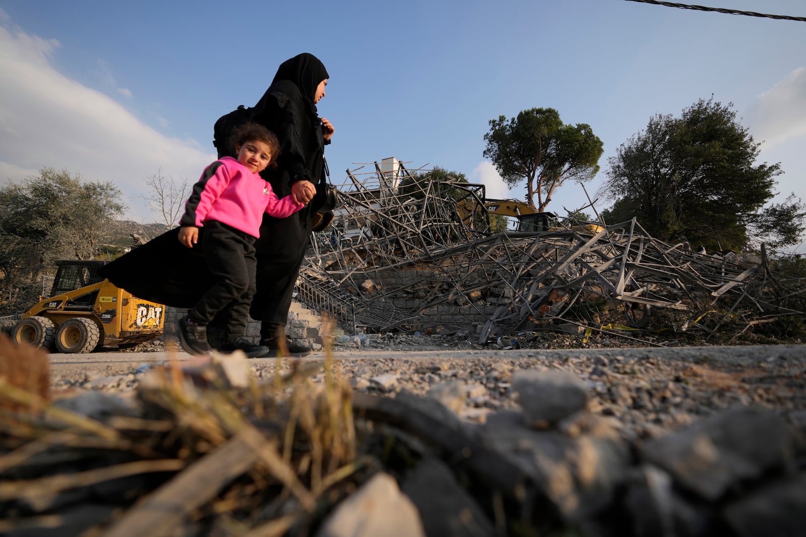 A woman with a child pass at the site where an Israeli airstrike hit a house in Aalmat village, northern Lebanon, Sunday, Nov. 10, 2024. (AP Photo/Hassan Ammar)