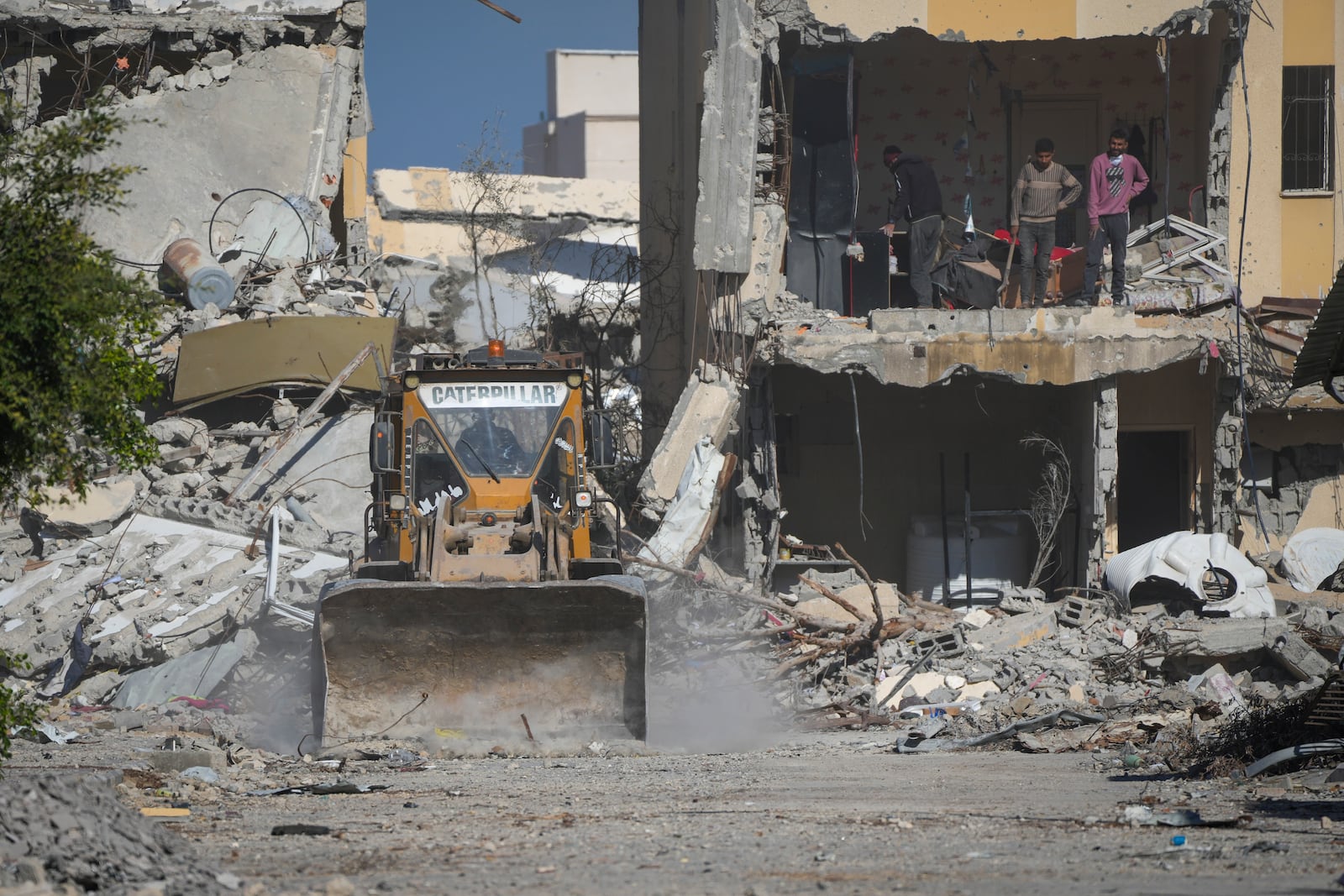 Palestinian youth watch as a bulldozer clears rubble from a street damaged by the Israeli air and ground offensive in Rafah, southern Gaza Strip, Tuesday, Jan. 21, 2025. (AP Photo/Abdel Kareem Hana)