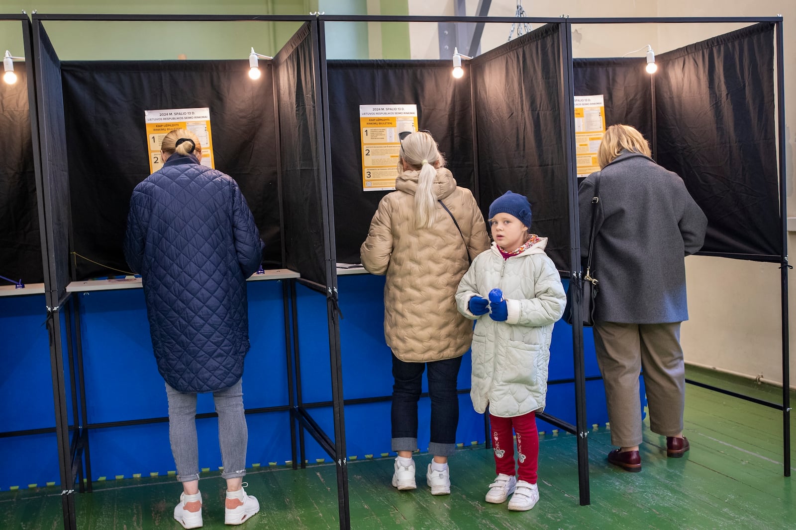 A girl looks from a voting booth as her relative fills-in a ballot at a polling station during the first round of voting in a parliamentary election, in Vilnius, Lithuania, Sunday, Oct. 13, 2024. (AP Photo/Mindaugas Kulbis)