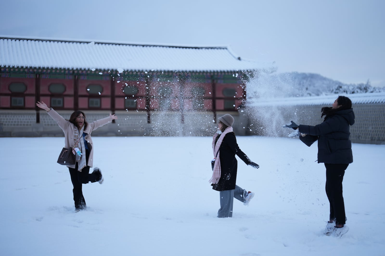 Visitors Cha, left, and Chie, center, from the Philippines, play with snow as they take selfies at the Gyeongbok Palace, one of South Korea's well-known landmarks, in Seoul, South Korea, Wednesday, Nov. 27, 2024. (AP Photo/Lee Jin-man)