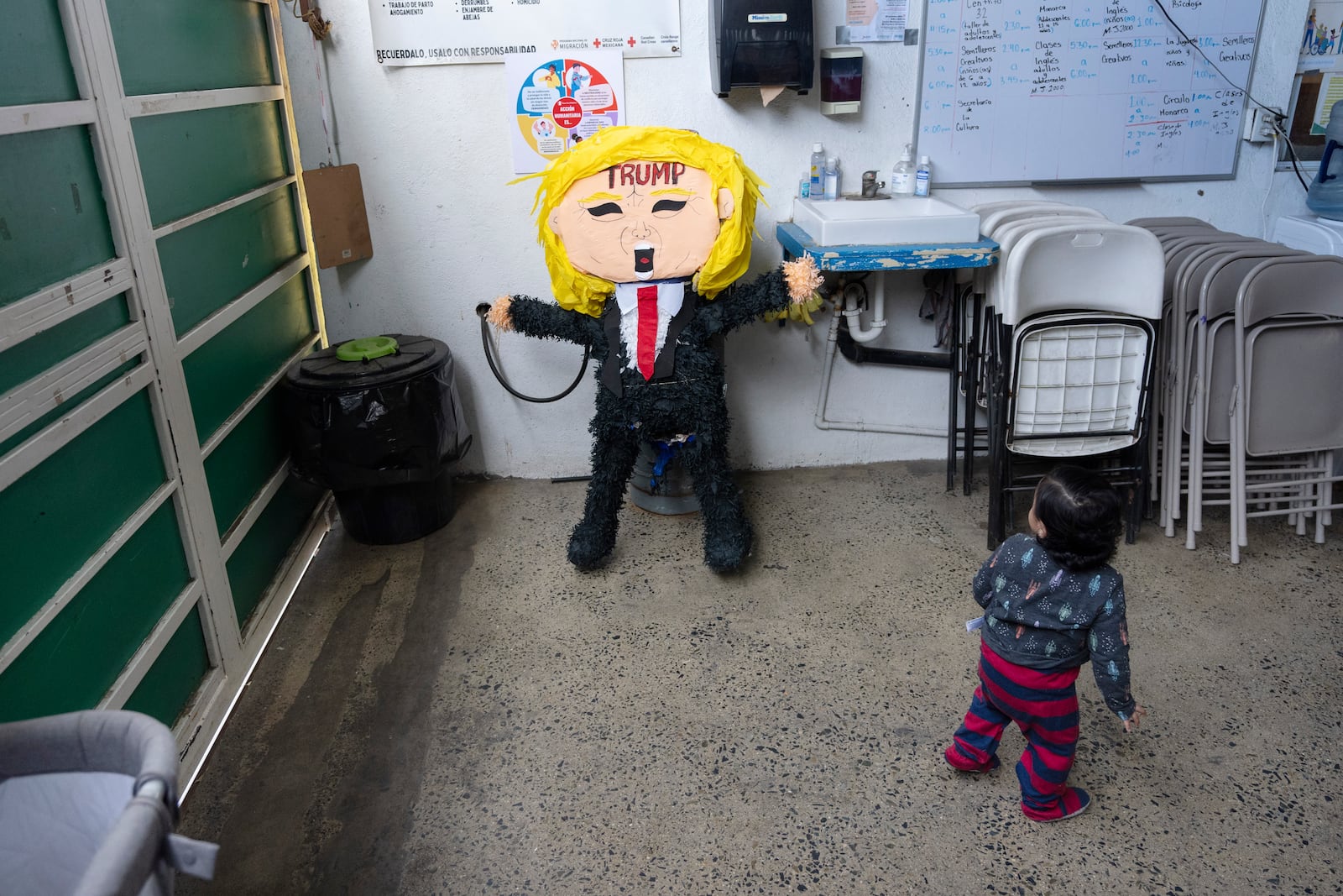 A child of a migrant family from the Mexican state of Guerrero looks at a piñata of President Donald Trump at a shelter for migrants Wednesday, Jan. 22, 2025, in the border city of Tijuana, Mexico. (AP Photo/Gregory Bull)