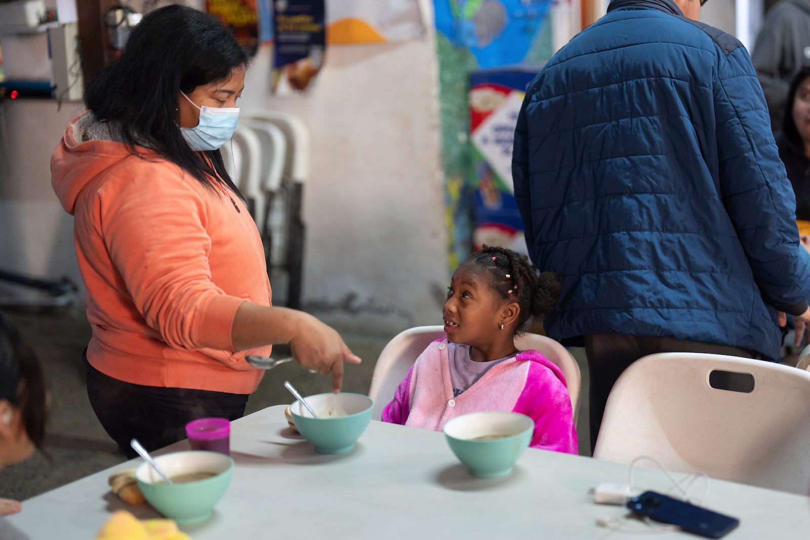 Maickeliys Rodriguez, 6, of Venezuela, right, cringes as her mother Margelis instructs her to eat breakfast at the migrant shelter they are staying at in Tijuana, Mexico, Saturday, Feb. 1, 2025. (AP Photo/Gregory Bull)