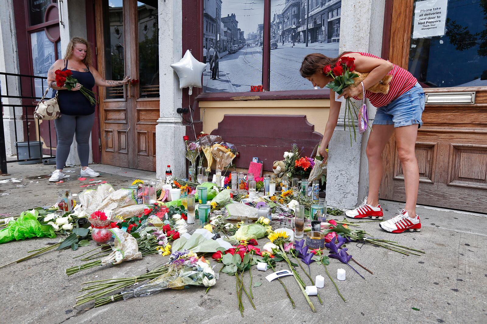 Natalie Driscoll, left, and Amber Lannon place flowers for shooting victim Derrick Fudge along East Fifth Street on Monday.  TY GREENLEES / STAFF