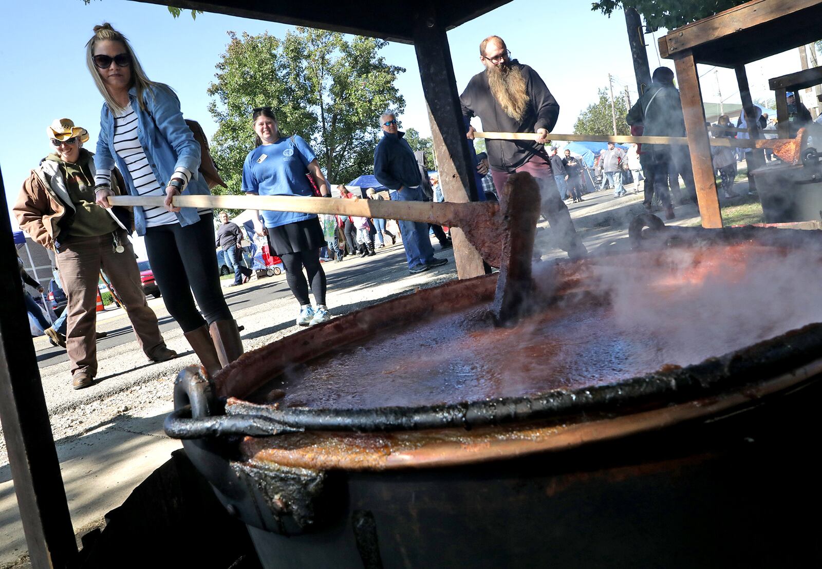 Shannon Webb takes a turn at stirring one of the giant kettles of apple butter cooking over an open fire at the 2019 Enon Apple Butter Festival. BILL LACKEY/STAFF