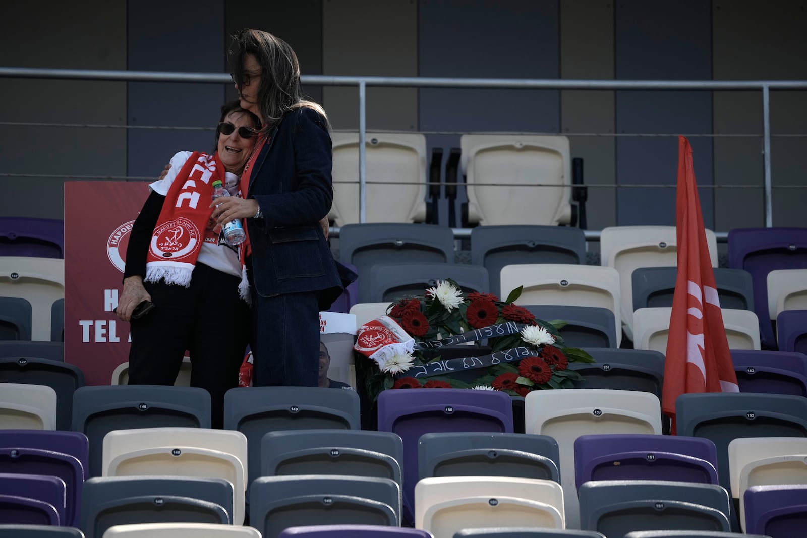 Dvora Idan, left, is comforted at a public memorial ceremony for her son, slain hostage Tsachi Idan, a fan of Hapoel Tel Aviv F.C., who was killed in Hamas captivity in the Gaza Strip, at Bloomfield Stadium in Tel Aviv, Israel, Friday, Feb. 28, 2025. (AP Photo/Leo Correa)