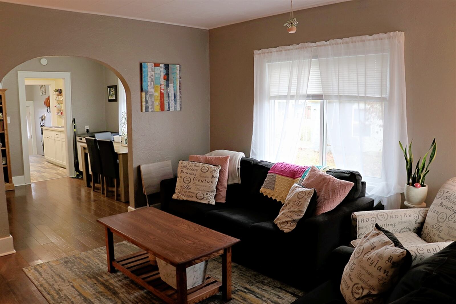 The living room features wood flooring and continues into the adjoining dining area. Textured walls have a fresh coat of neutral color paint.