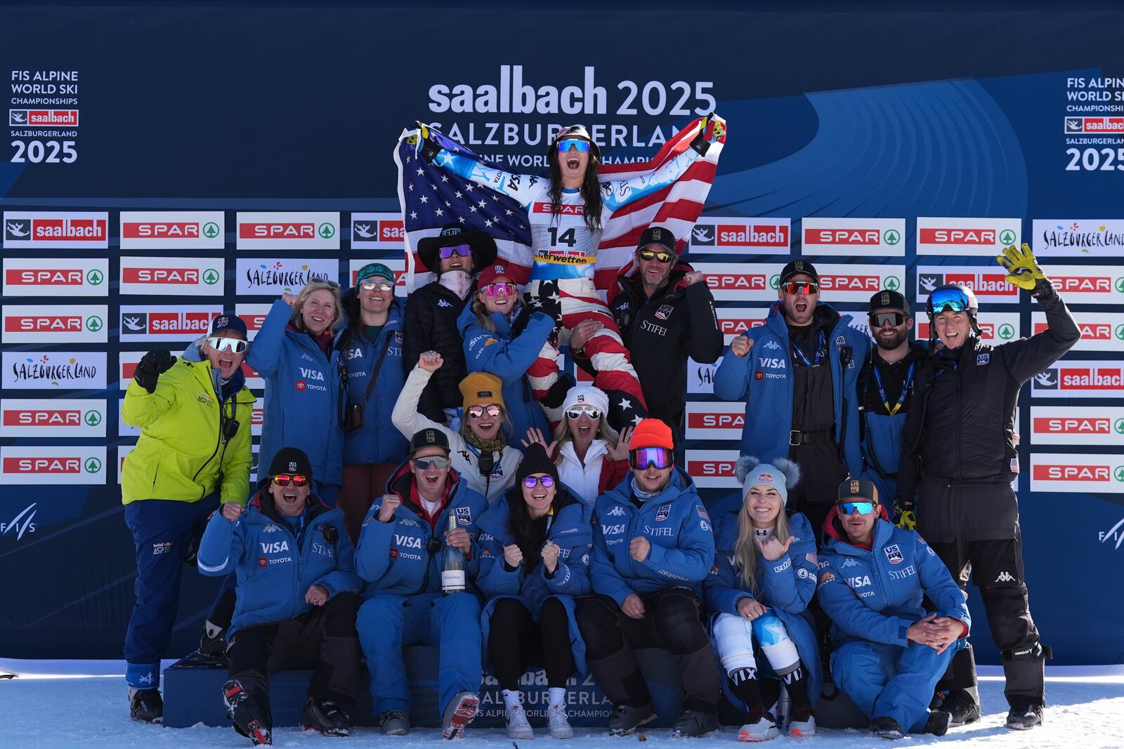 United States' Lauren Macuga, top, celebrates on the podium with the team, including United States' Lindsey Vonn, bottom right, after taking joint third place in a women's Super-G, at the Alpine Ski World Championships, in Saalbach-Hinterglemm, Austria, Thursday, Feb. 6, 2025. (AP Photo/Giovanni Auletta)