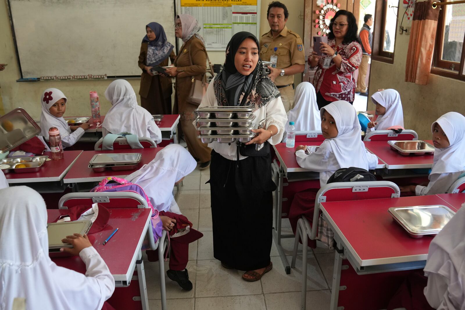 A member of school committee distributes meals to students during the kick off of President Prabowo Subianto's ambitious free meal program to feed children and pregnant women nationwide despite critics saying that its required logistics could hurt Indonesia's state finances and economy, at an elementary school in Depok, West Java, Indonesia, Monday, Jan. 6, 2025. (AP Photo/Dita Alangkara)