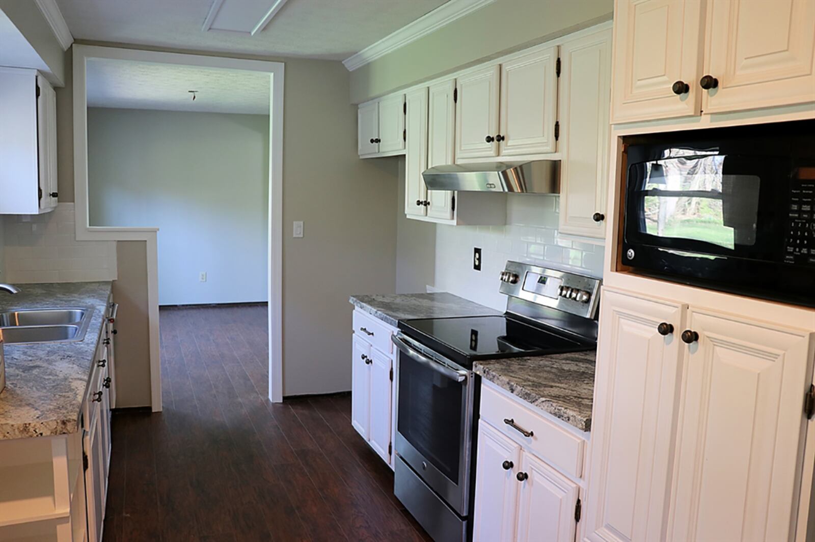 Connecting the family room to the dining room, the galley kitchen has white cabinetry and solid-surface countertops. There is a double sink below a window and open shelves near the breakfast nook. CONTRIBUTED PHOTOS BY KATHY TYLER