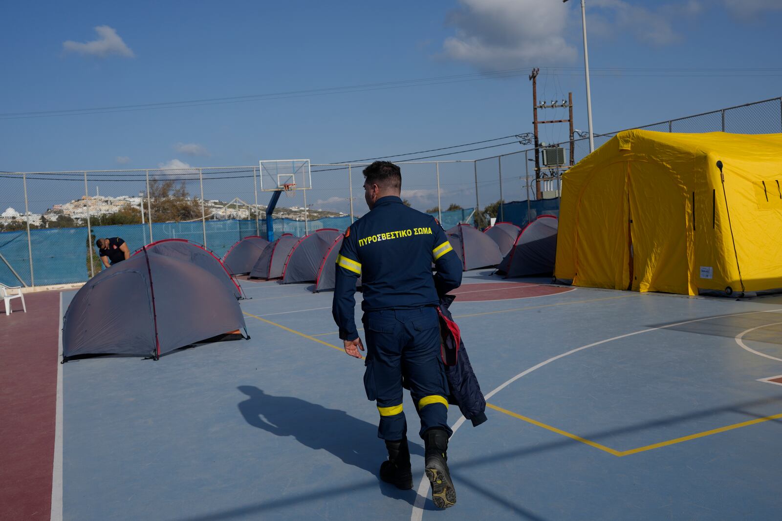 A firefighter walks next to tents set up at a basketball court to accommodate Fire Service rescuers as Greek authorities is taking emergency measures in response to intense seismic activity on the popular Aegean Sea holiday island of Santorini, southern Greece, Monday, Feb. 3, 2025. (AP Photo/Petros Giannakouris)