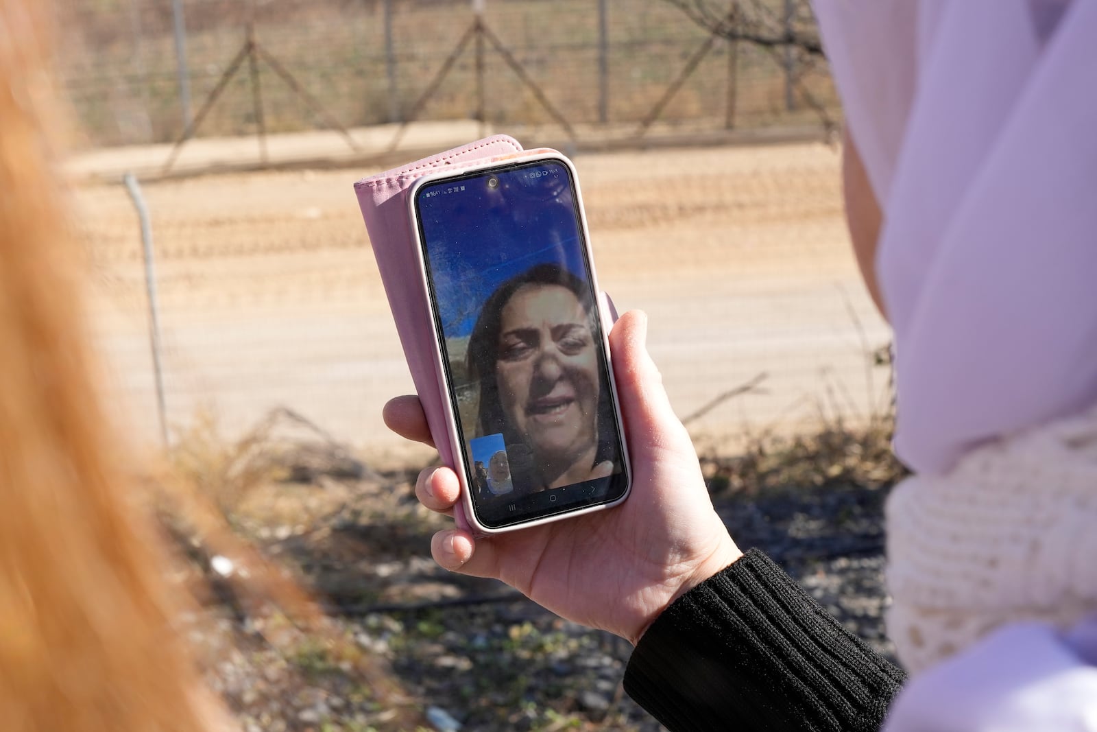 Samar Safadi holds her phone as she talks by video call with her sister, Sawsan, who lives inside the buffer zone near the "Alpha Line" that separates the Israeli-controlled Golan Heights from Syria, in the town of Majdal Shams, Wednesday, Dec. 18, 2024. (AP Photo/Matias Delacroix)