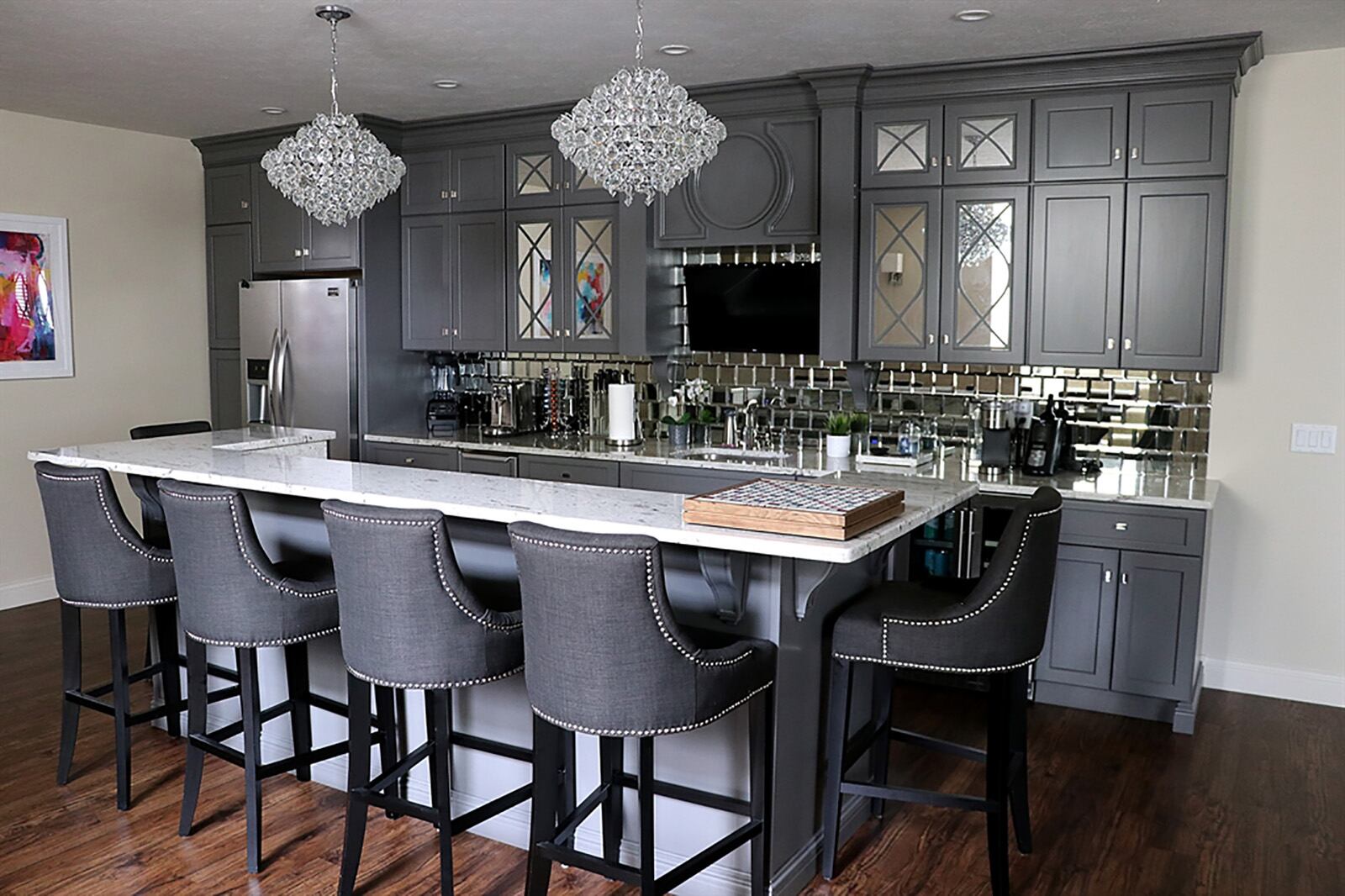 The lower level is a combination recreation room, family room and game room with the centerpiece being the wet bar area with mirrored tile backsplash, gray cabinetry with mirrored-glass panel doors and crystal hanging light fixtures. CONTRIBUTED PHOTO BY KATHY TYLER