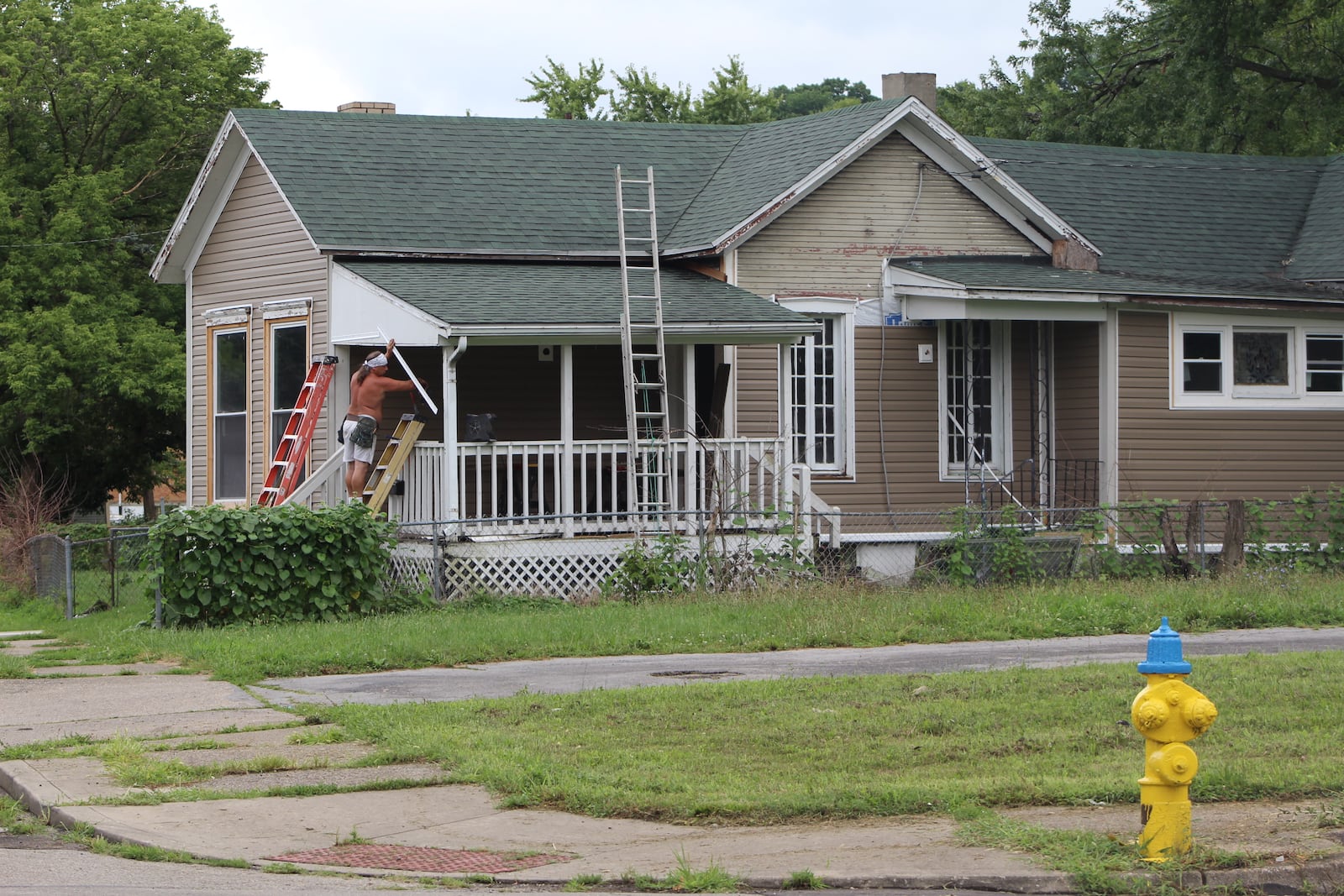 A man works on the exterior of a home on Hawker Street in the Twin Towers neighborhood. The home is next to a vacant lot that the city of Dayton owns. The city owns several empty lots on that street. CORNELIUS FROLIK / STAFF