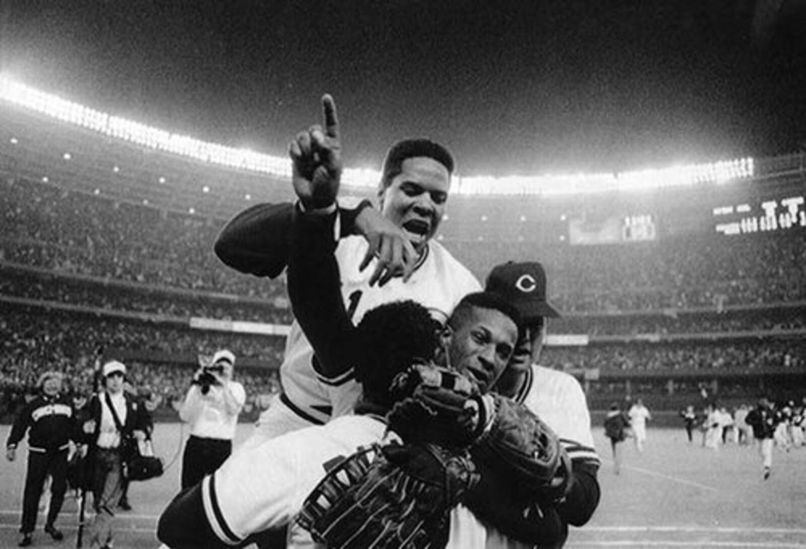 Barry Larkin dives over top while Eric Davis hugs teammates. Cincinnati Reds beat Pirates to gain spot in World Series. First Reds appearance in World series since 1976.