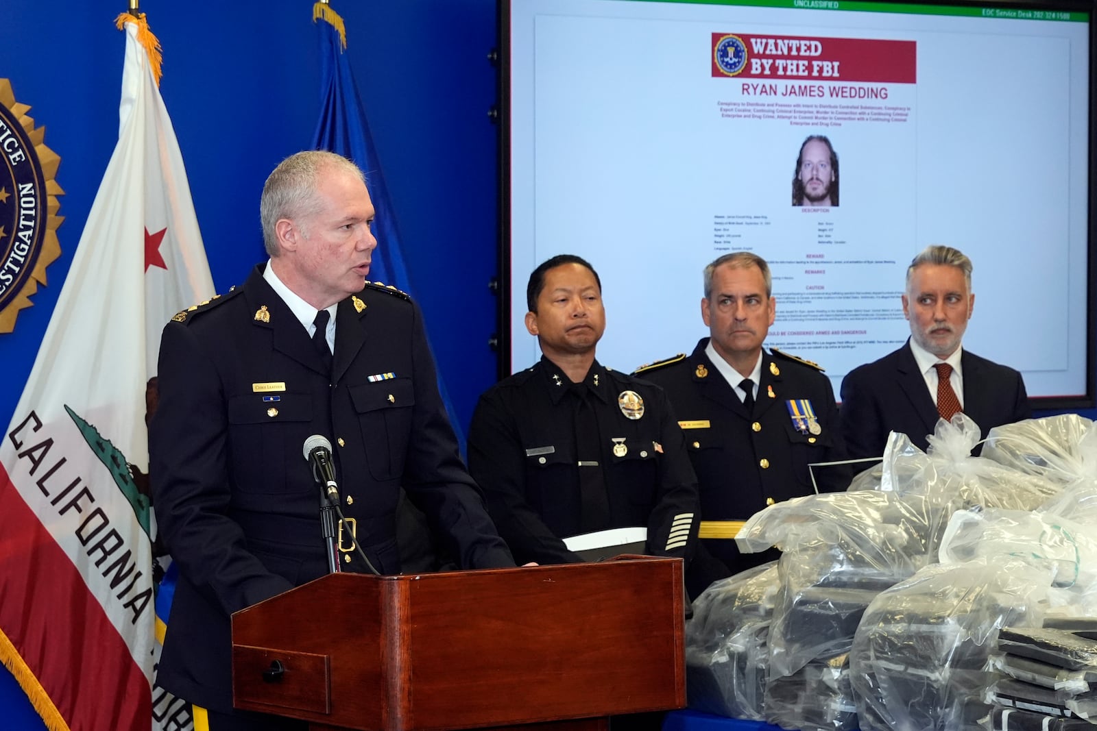 Chris Leather, chief superintendent with the Royal Canadian Mounted Police, at podium, joined by U.S.. federal, local, and international officials, announces federal charges and arrests of alleged members of a transnational drug trafficking operation that routinely shipped hundreds of kilograms of cocaine from Colombia, through Mexico and Southern California, to Canada and other locations in the United States, during a news conference at the FBI offices in Los Angeles, Thursday, Oct. 17, 2024. (AP Photo/Damian Dovarganes)