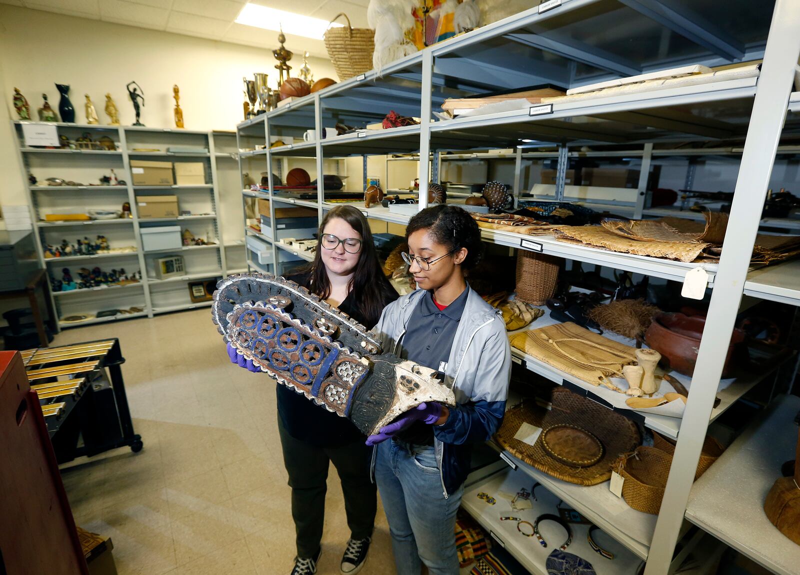 Abbey Search (left) and Asia Adomanis, interns at the National Afro-American Museum & Cultural Center in Wilberforce, look at head dress that is part of the museum's ethnographic collection, in one of the objects collections storage rooms. Just a fraction of the museum's collection- like most museums - is on display at any time, the majority is stored in archives. LISA POWELL / STAFF