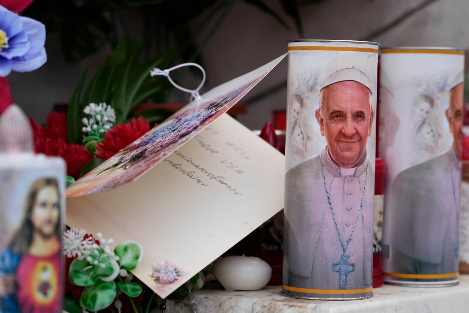 Candles with the pictures of Pope Francis are the laid under the statue of late Pope John Paul II outside Agostino Gemelli Polyclinic in Rome, Wednesday, Feb. 19, 2025, where the Pontiff is hospitalized since Friday, Feb. 14. (AP Photo/Gregorio Borgia)