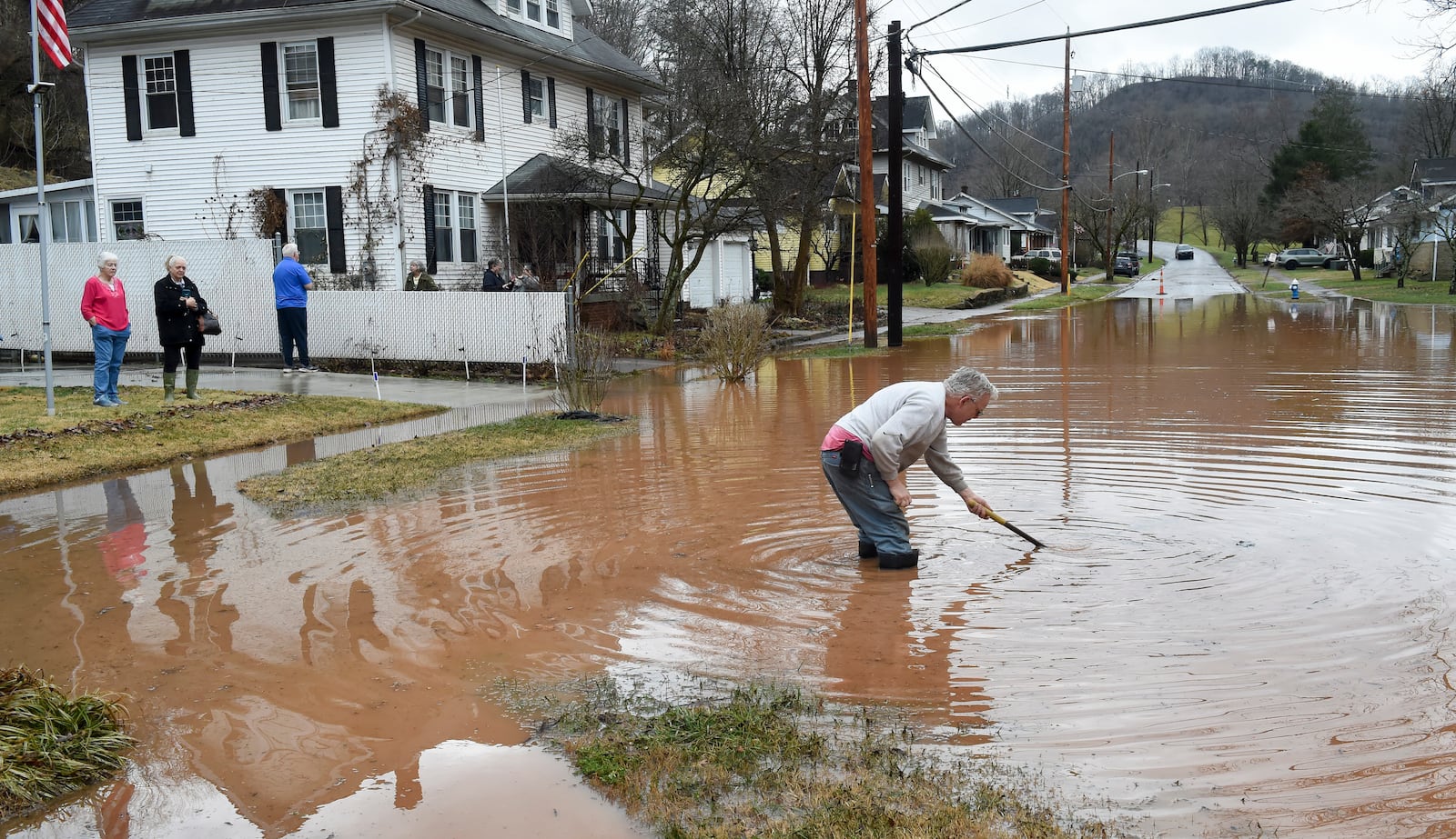 Harry Miller works to open a clogged sewer drain near his house in Nitro, W.Va., as his neighbors look on Thursday, Feb. 6, 2025. (Chris Dorst/Charleston Gazette-Mail via AP)