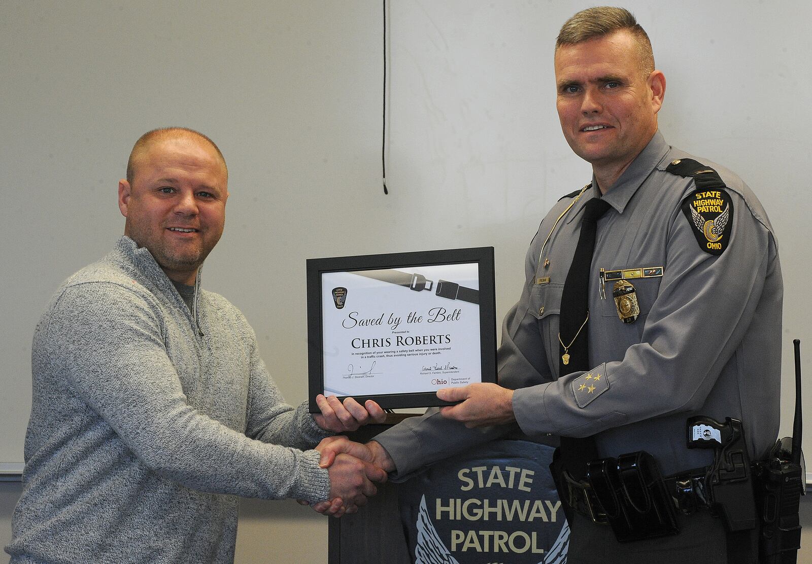 Chris Roberts of Moraine and his 2-year-old son Colton were presented with a "Saved by the Belt" certificate from Ohio State Highway Patrol Lt. Geoffrey Freeman Monday, Nov. 1, 2021. Chris Roberts wore his seat belt and his young son was strapped in a child safety seat, which saved them from life-threatening injuries when they were struck by another car Oct. 3 on Interstate 75 in Dayton. MARSHALL GORBY/STAFF