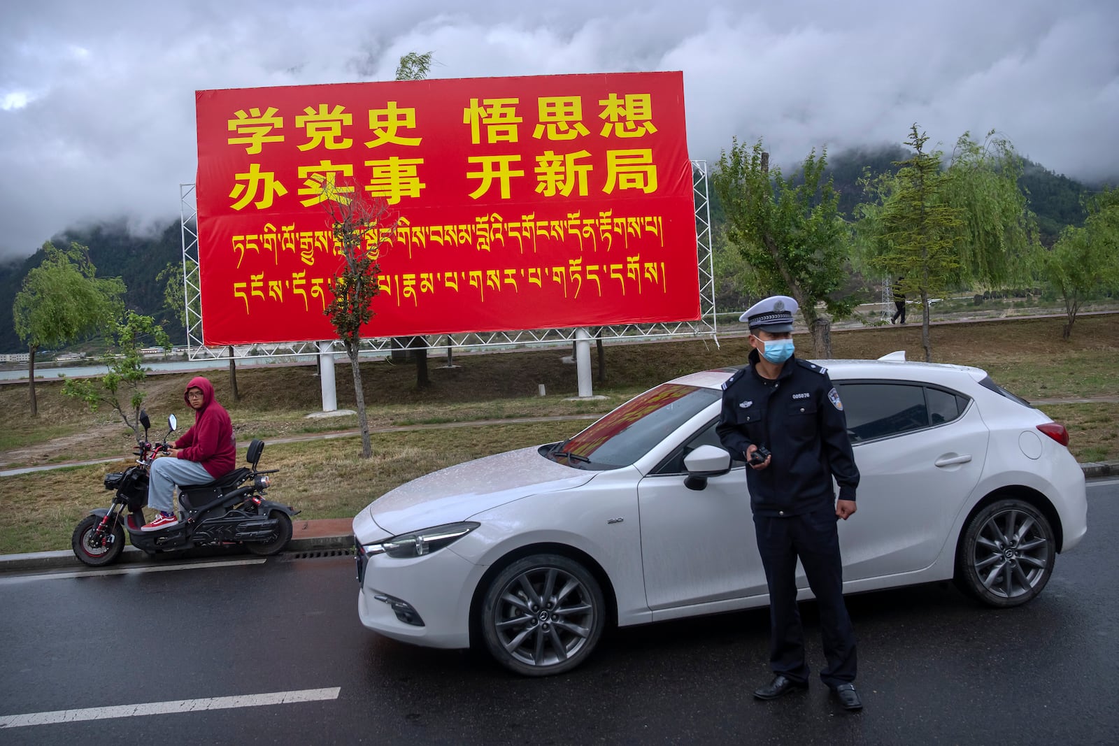 FILE - A police officer directs traffic near a billboard that reads in Chinese "Study Communist Party history, understand its theories, do practical work, and make new advances" in Nyingchi in western China's Tibet Autonomous Region, as seen during a rare government-led tour of the region for foreign journalists, June 4, 2021. (AP Photo/Mark Schiefelbein, File)