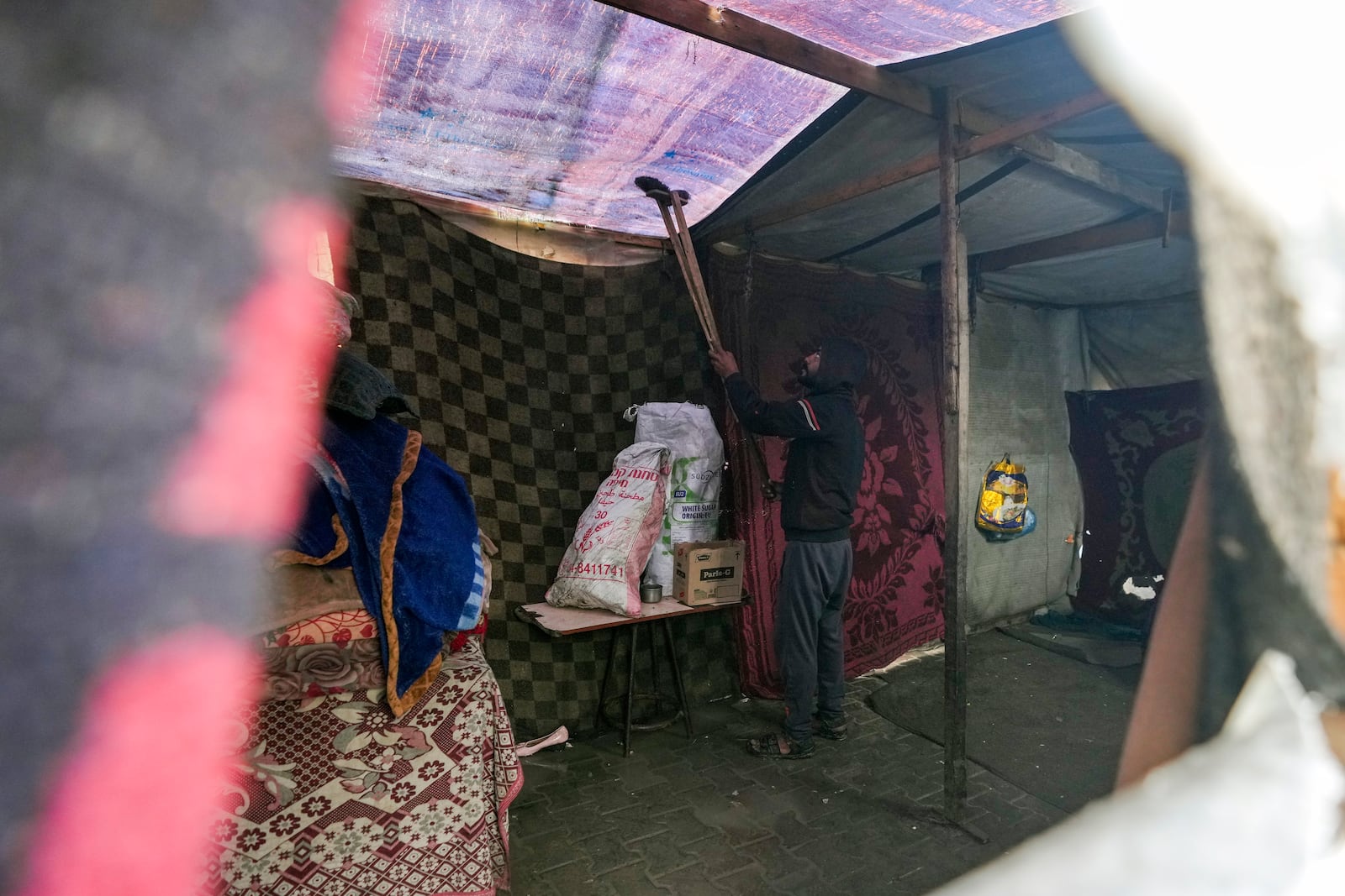 A man removes water from the fabric roof of a makeshift tent following overnight rainfall at the refugee tent camp for displaced Palestinians in Deir al-Balah, central Gaza Strip, Tuesday, Dec. 31, 2024. (AP Photo/Abdel Kareem Hana)