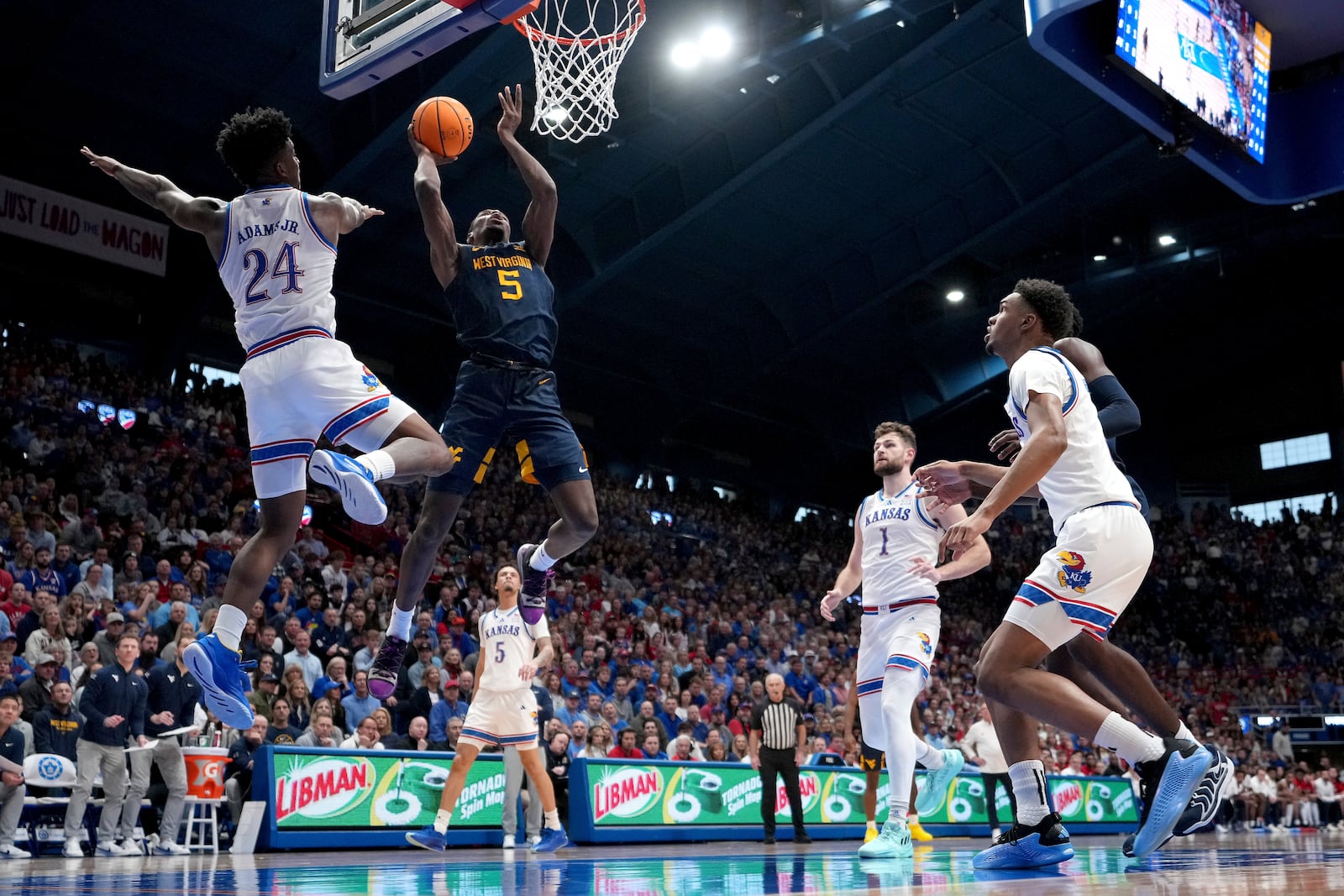 West Virginia guard Toby Okani (5) gets past Kansas forward KJ Adams Jr. (24) to put up a shot during the second half of an NCAA college basketball game, Tuesday, Dec. 31, 2024, in Lawrence, Kan. West Virginia won 62-61(AP Photo/Charlie Riedel)