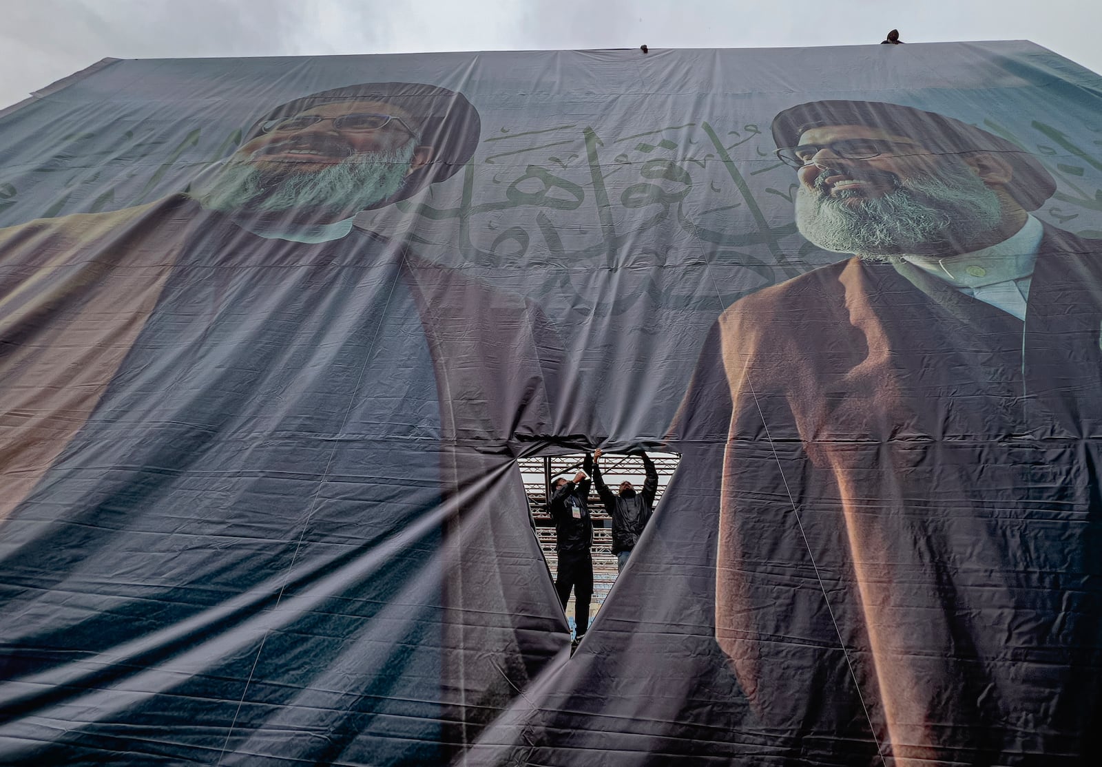 Workers display a giant banner with the portraits of the late Hezbollah leaders Sayyed Hassan Nasrallah, left, and Sayyed Hashem Safieddine, during preparation, a day ahead of their funeral procession at Beirut's City Sportive stadium, in Beirut, Lebanon, Saturday, Feb. 22, 2025. (AP Photo/Hussein Malla)